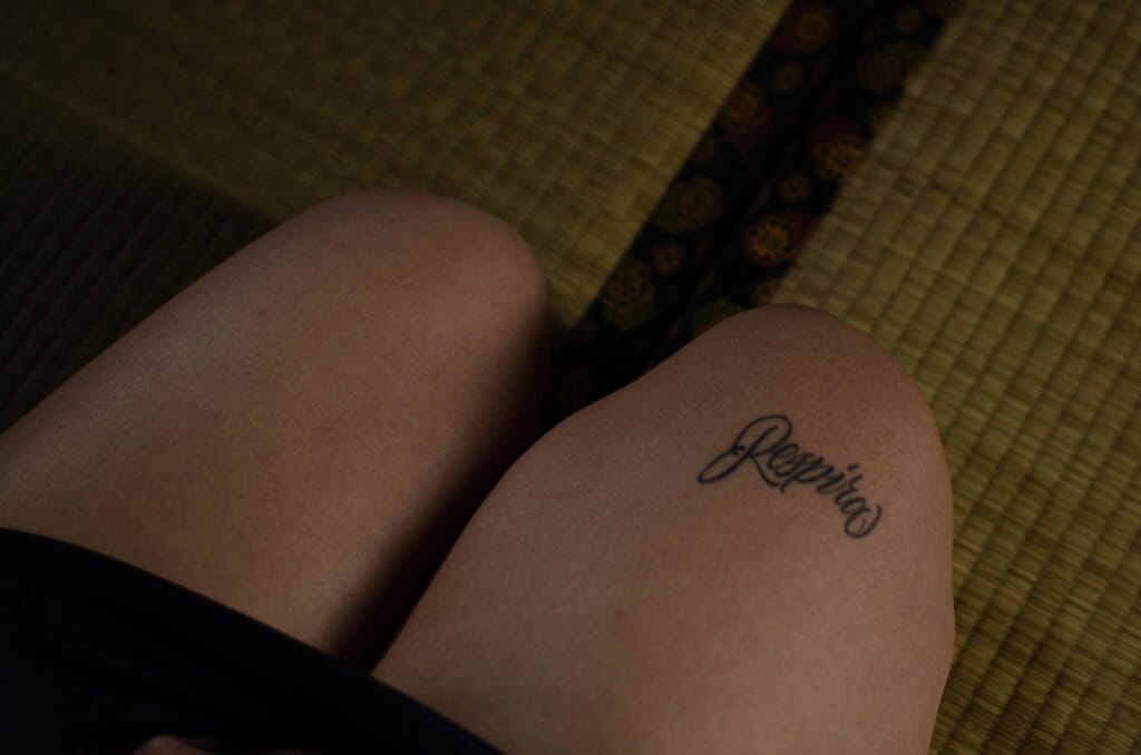 Dettaglio delle ginocchia di Marta Tenshiko sul tatami con il tatuaggio Respira