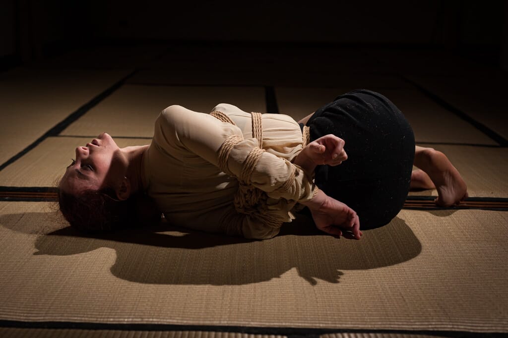 Marta distesa sul fianco dopo la sospensione con le braccia ancora raccolte, nella progressione di kinbaku