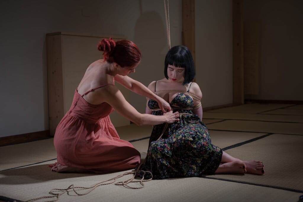 Tenshiko seduta accanto a Elettris mentre inizia la legatura sul tatami