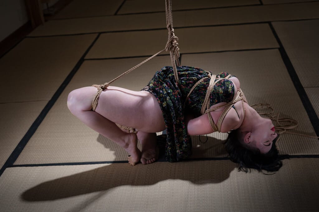 Elettris ruota nella sospensione mentre una gamba scende verso il tatami, nella progressione di kinbaku