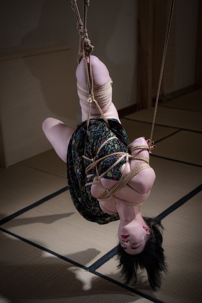 Vista ravvicinata di Elettris nella sospensione capovolta con il vestito floreale sospeso, nella progressione di kinbaku