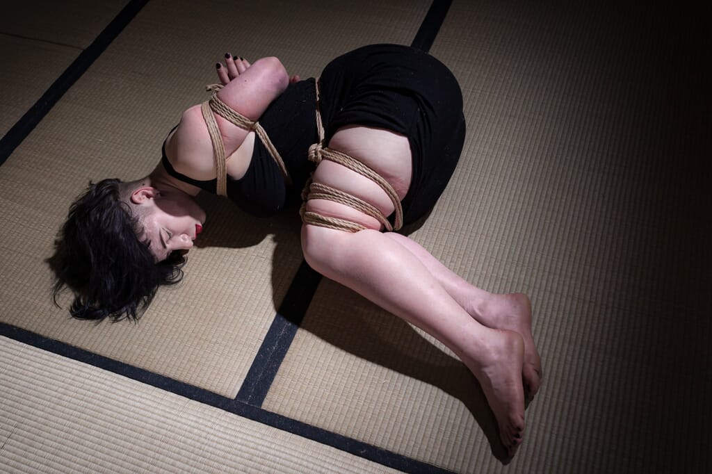 Elettris distesa e raccolta sul tatami, ancora avvolta dalle corde dopo la sospensione, nel contesto del kinbaku