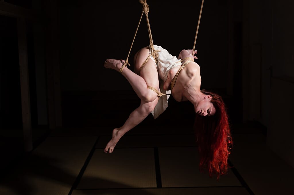 Marta Tenshiko in a side suspension with her legs arranged along asymmetrical lines, within a kinbaku session