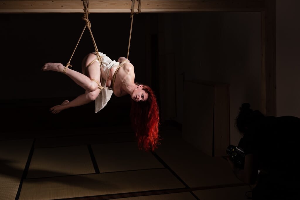 Marta Tenshiko in an inverted side suspension, supported by vertical rope lines, in the kinbaku progression