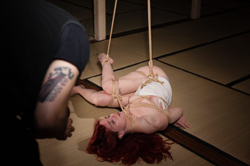 A transitional moment in the semenawa with Marta Tenshiko on the floor and the ropes under tension