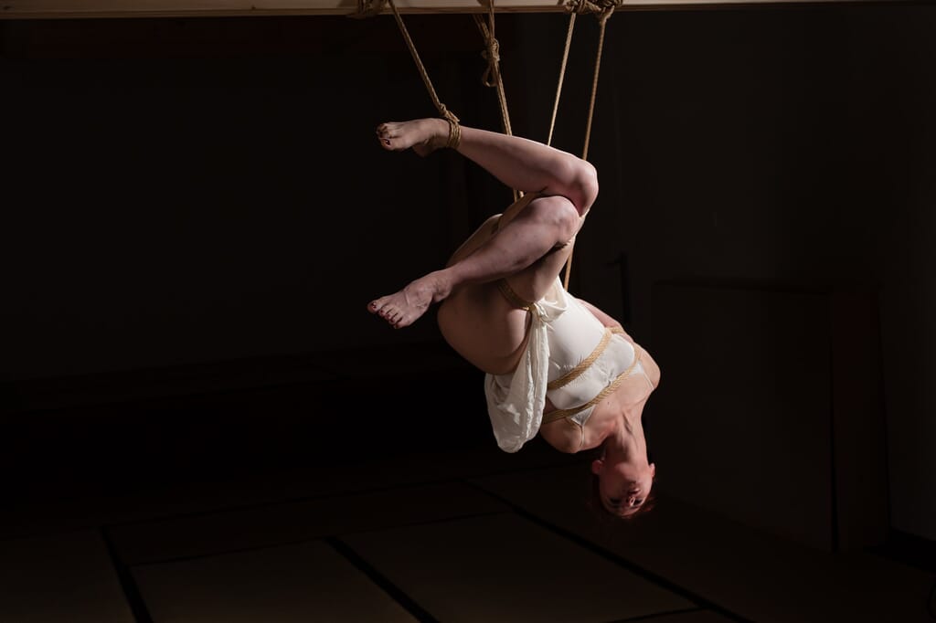 Marta Tenshiko inverted in suspension, with one leg folded and the other opening into space
