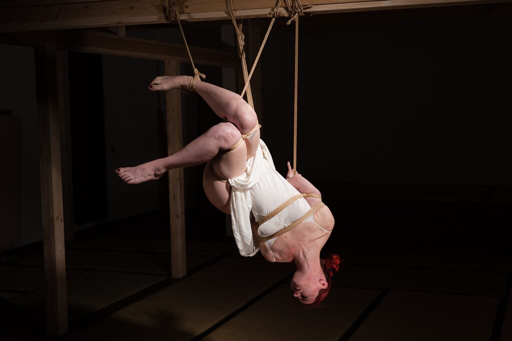 Close view of Marta Tenshiko inverted, with her legs open in an asymmetrical pose