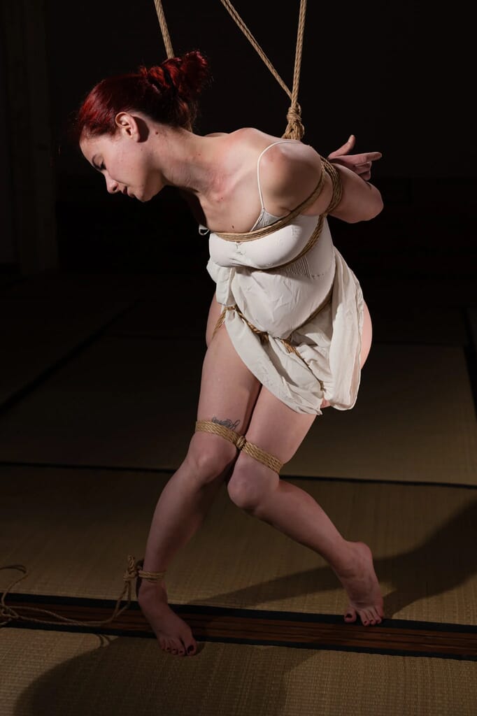 Marta Tenshiko leaning forward under rope tension, with her arms tied behind her, in the most intense phase of the semenawa session
