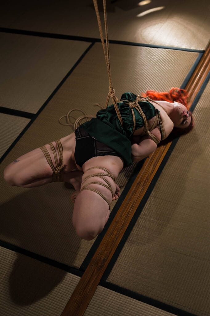 Dettaglio dal basso del chest piece e della gamba sollevata di Marta Tenshiko, nel contesto del kinbaku