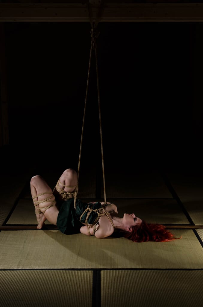Marta Tenshiko distesa sul fianco, ancora collegata alle linee di sospensione, nella progressione di kinbaku